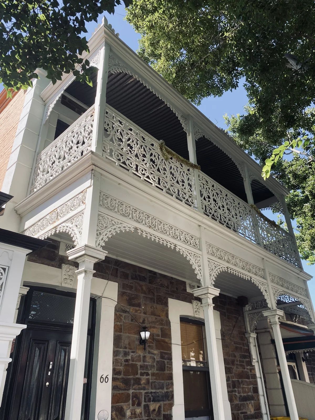 A two-storey Adelaide bluestone terrace with cast-iron lacework and dressed sandstone quoins around the openings.